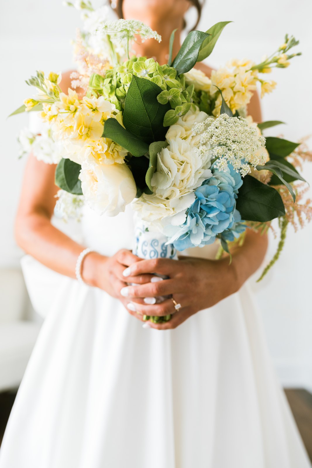 A bride holding a Flower Girl Studio bouquet of white, cream, and blue flowers