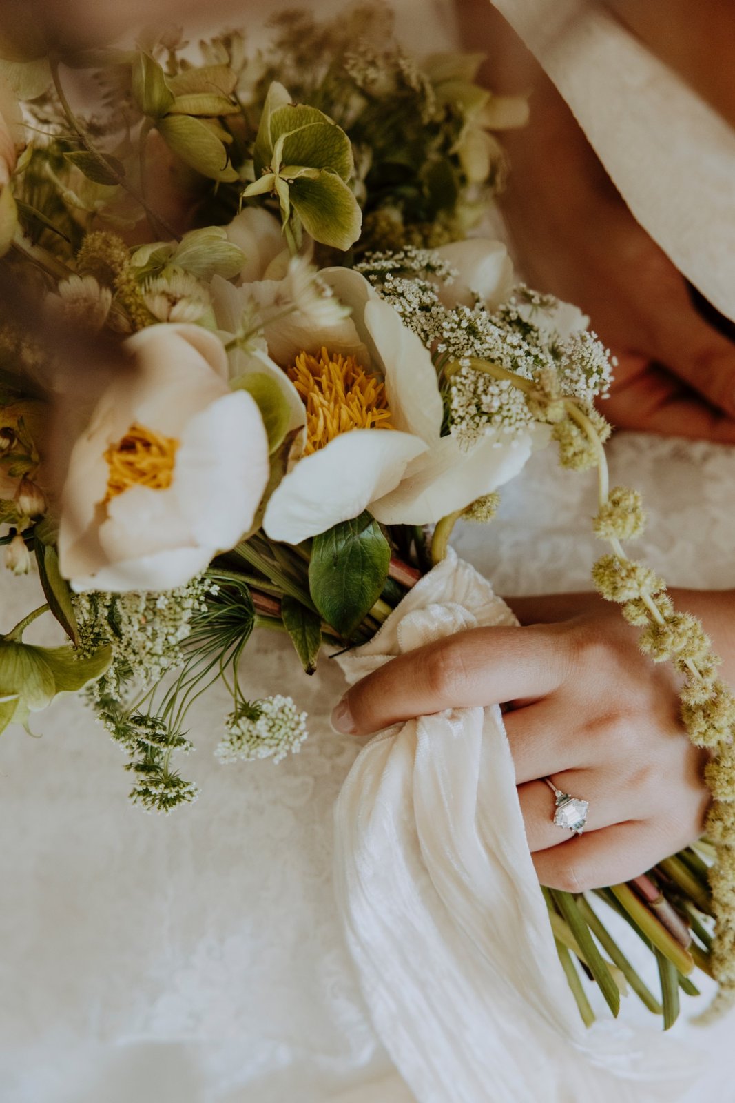 A bride holding a bouquet of white peonies, hellebores, and Queen Anne's lace tied with a silk ribbon